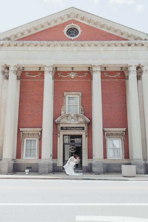 Bride in white dress exits red brick building with white columns.