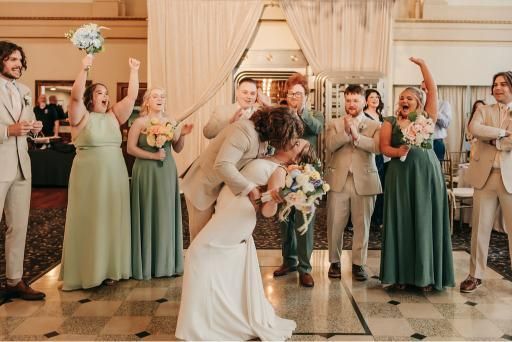 Bride and groom share a kiss as wedding party cheers in a bright, decorated room.