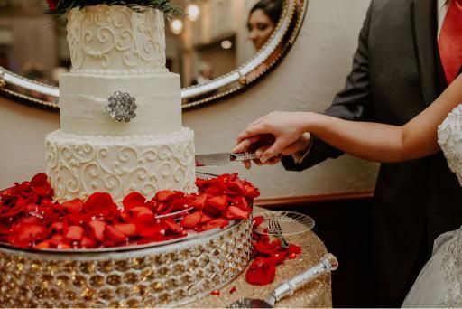 Bride and groom cutting a tiered wedding cake decorated with red rose petals.