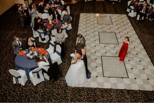 Wedding reception: Bride and groom dance on a checkered floor; guests watch at tables in a banquet hall.