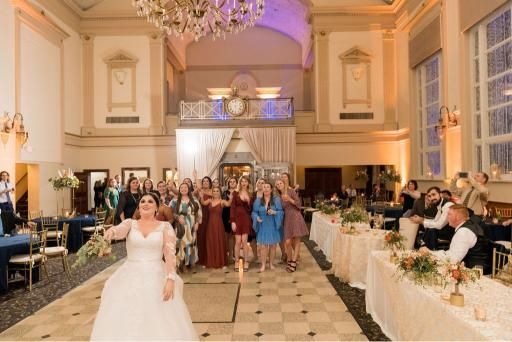 Bride throwing bouquet to a group of women at an elegant wedding reception.