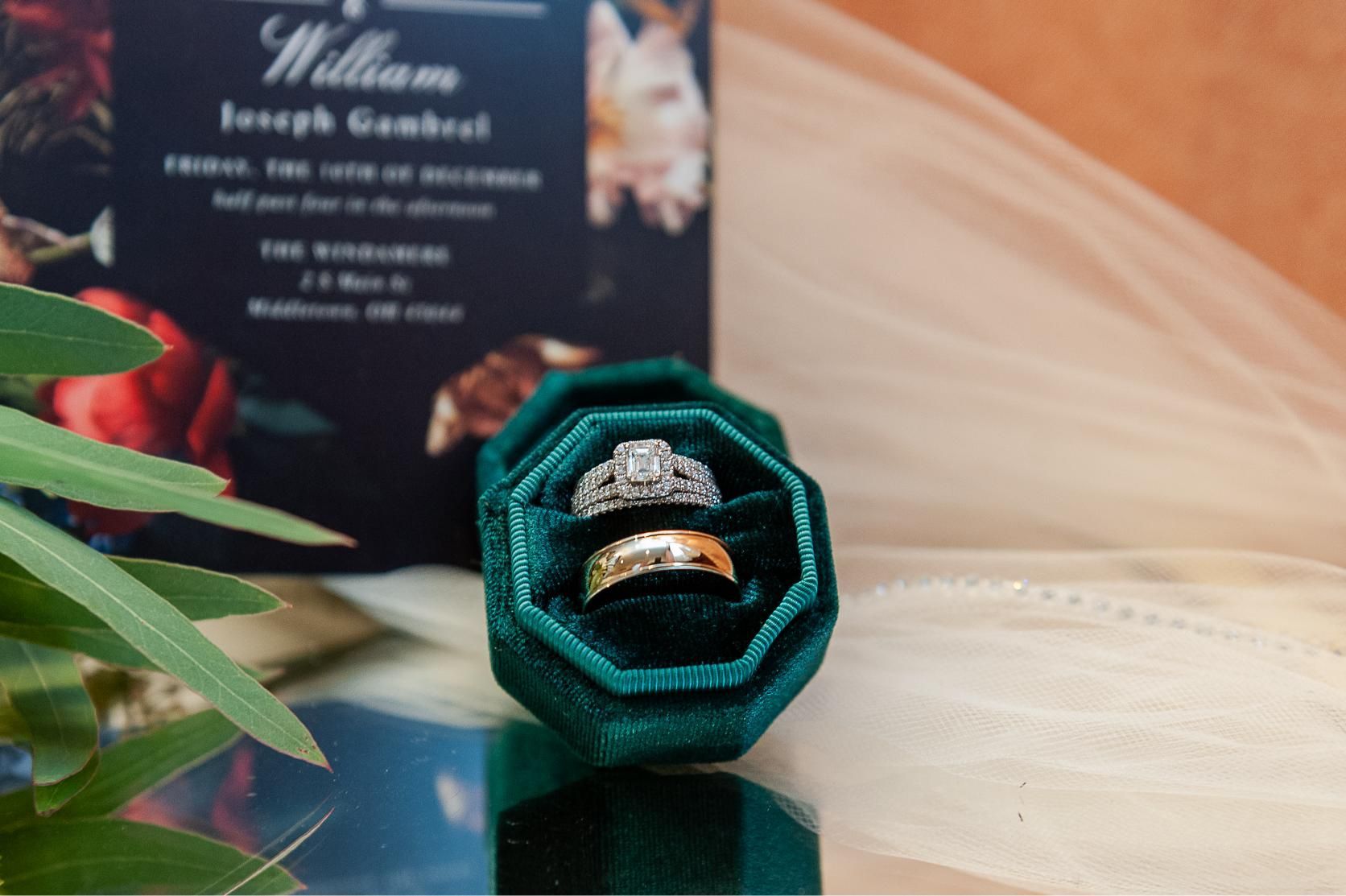 Wedding rings in a green velvet box with invitation in the background.
