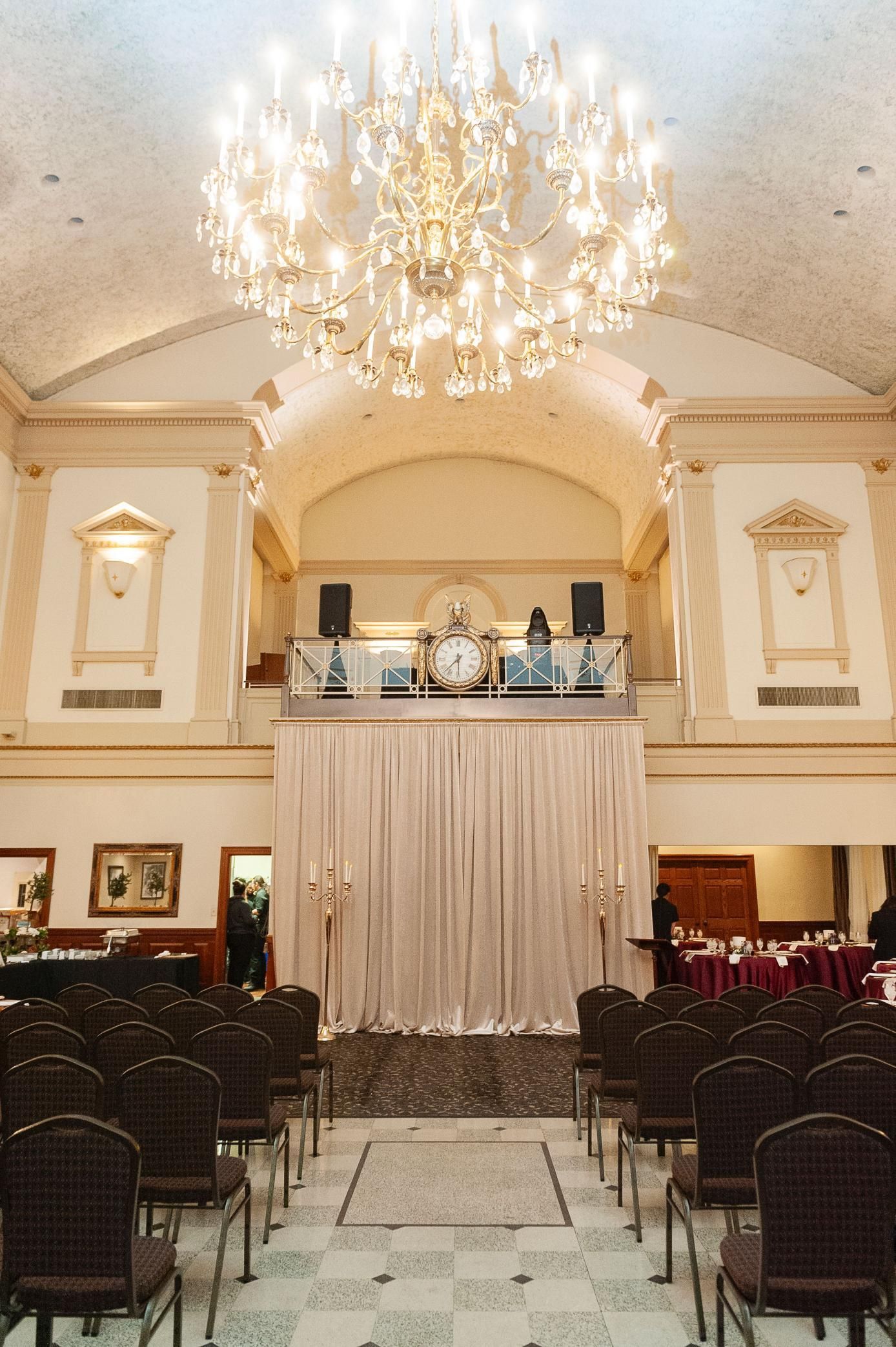 Wedding venue with draped stage, rows of chairs, and a large chandelier.