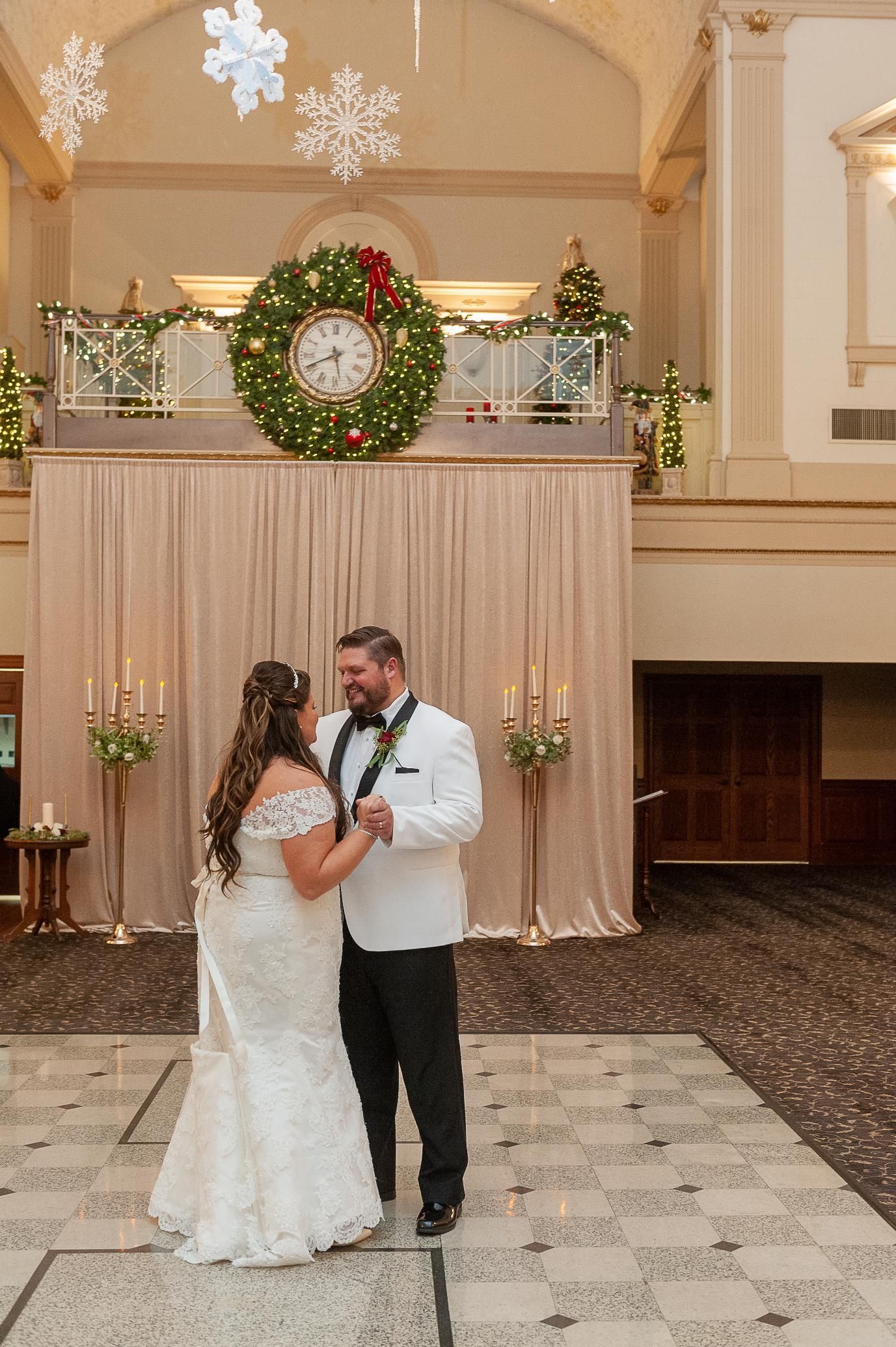 Bride and groom dancing at wedding reception. Bride in white lace dress, groom in tuxedo. Festive decorations.