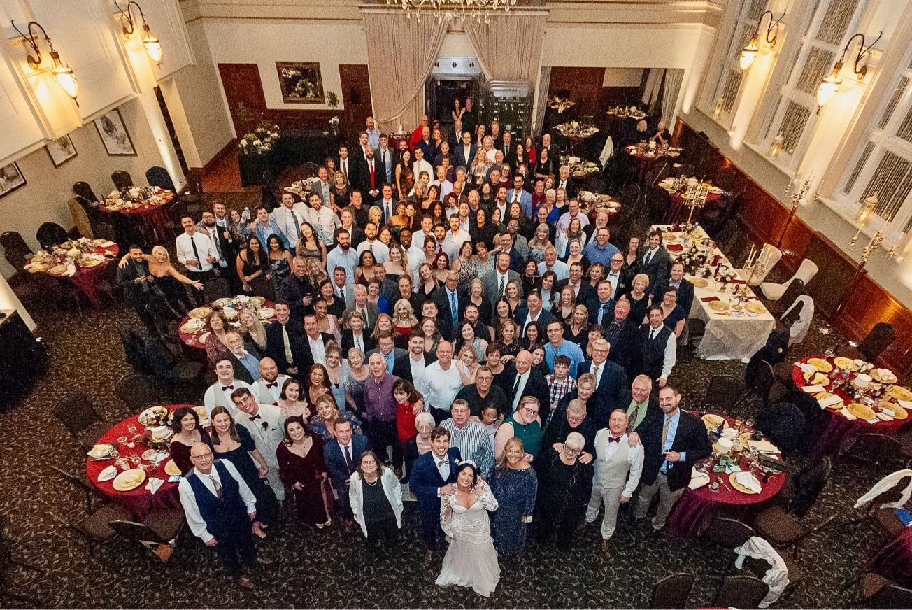 Large group of people gathered for an event in a banquet hall. Many smiling.