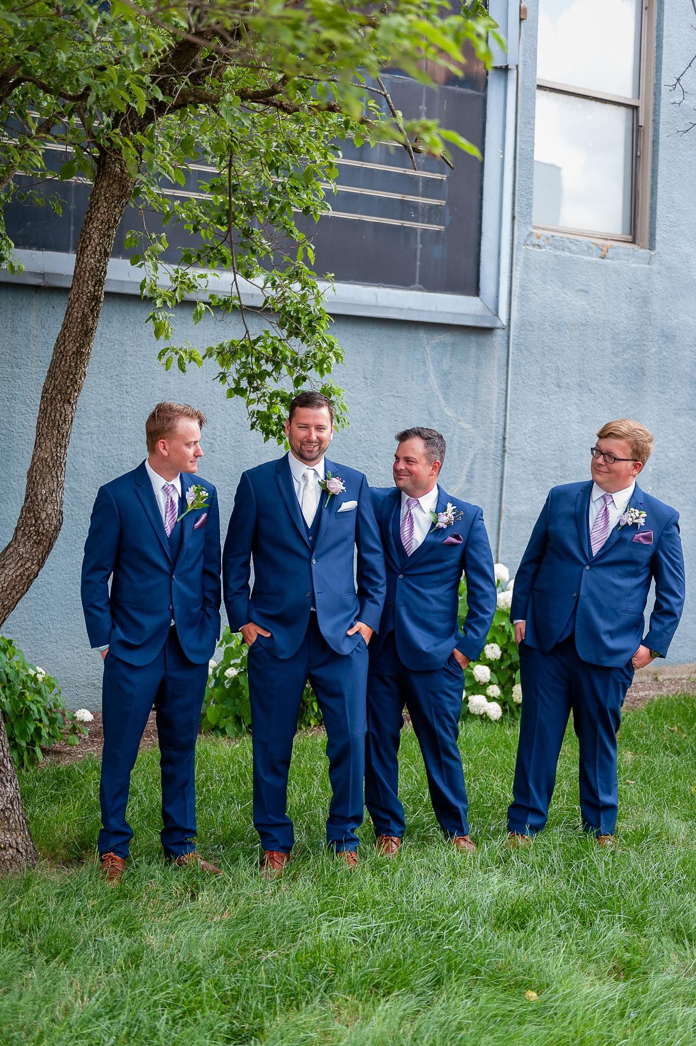 Four men in blue suits stand outside, smiling.