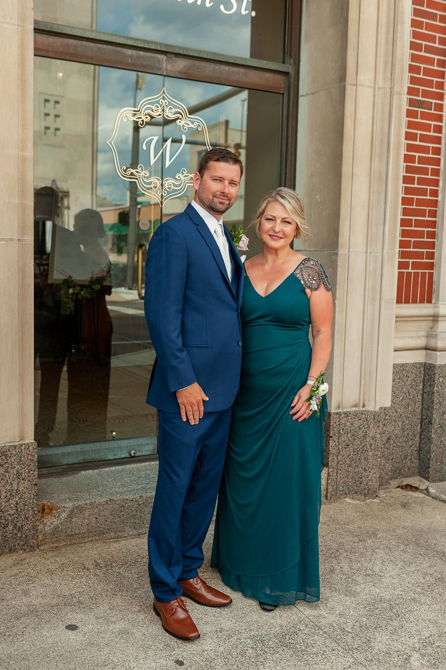 A man in a blue suit and a woman in a green dress pose together outside.