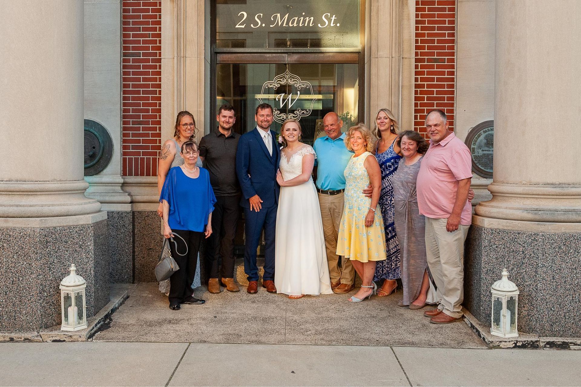 Group of people posing for a photo outside a building with a wedding couple in the center.