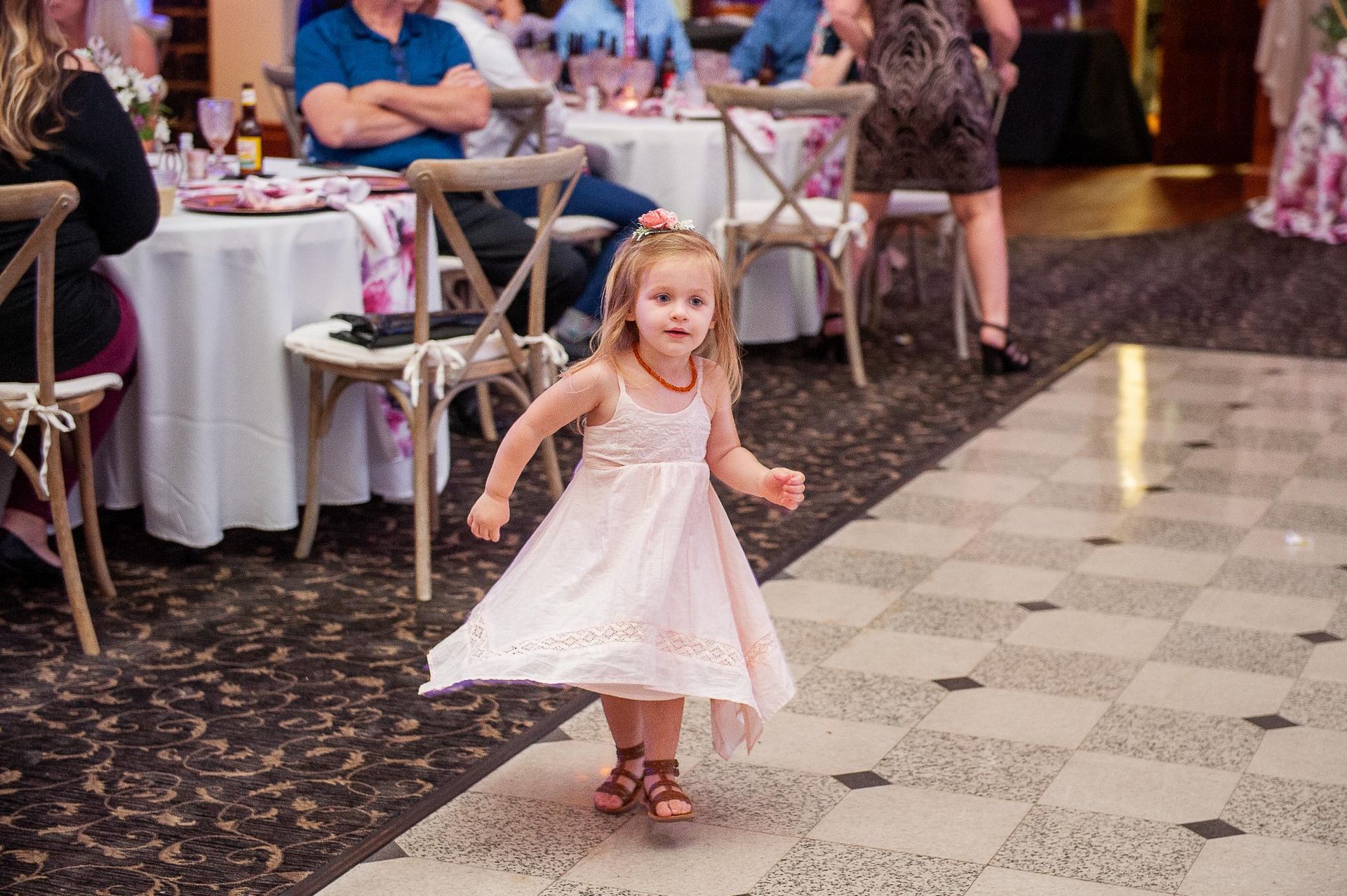 Young girl in a pink dress dances on checkered floor at a wedding reception.