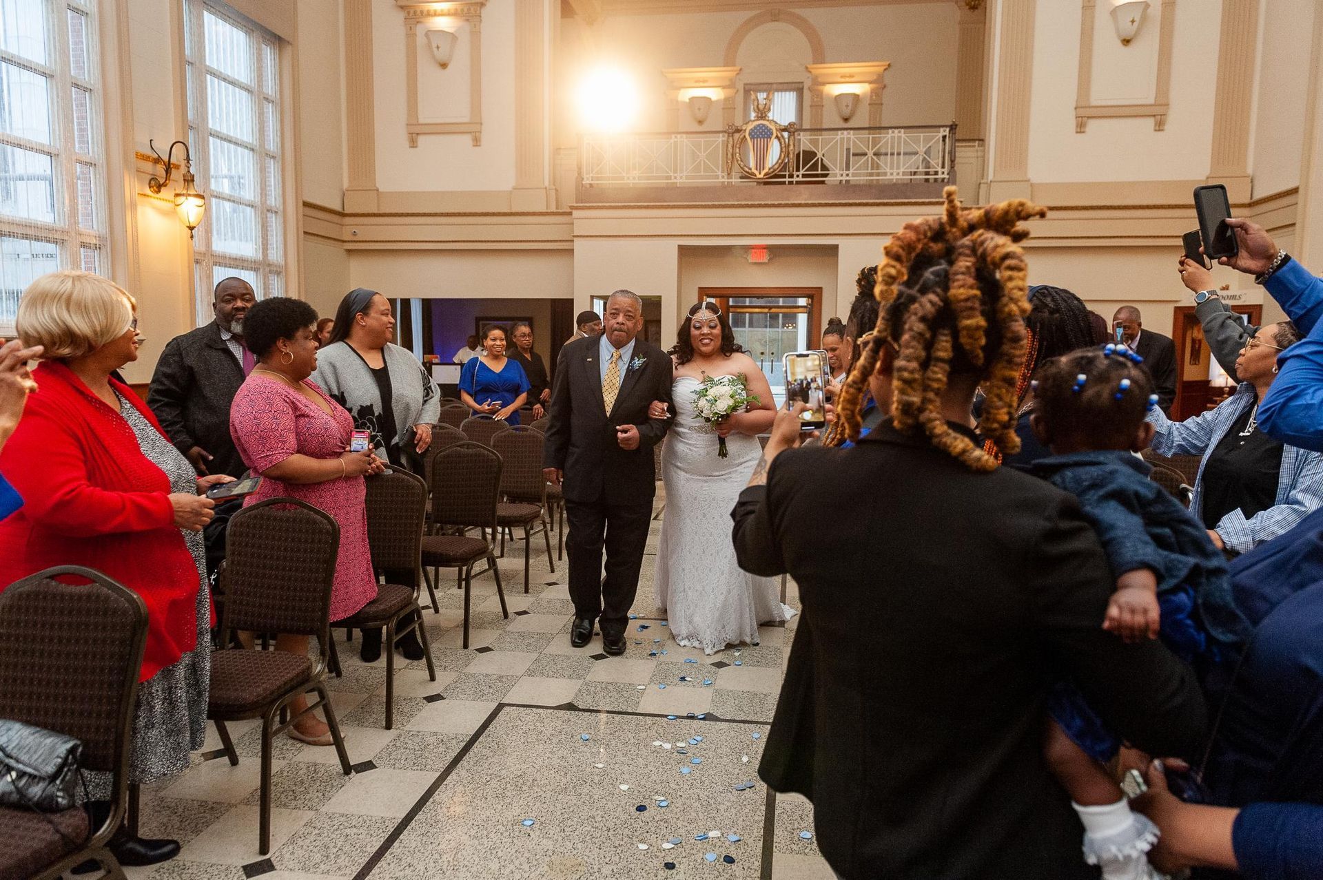 Bride walks down the aisle with her father, surrounded by guests, at a wedding ceremony.