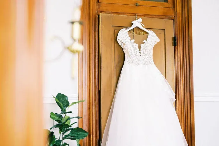 Wedding dress hanging on a wooden door with a white lace bodice and flowing tulle skirt.