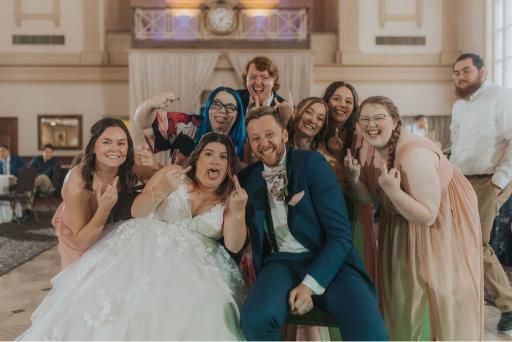 Wedding party celebrating, bride and groom center, many holding up middle fingers, venue.