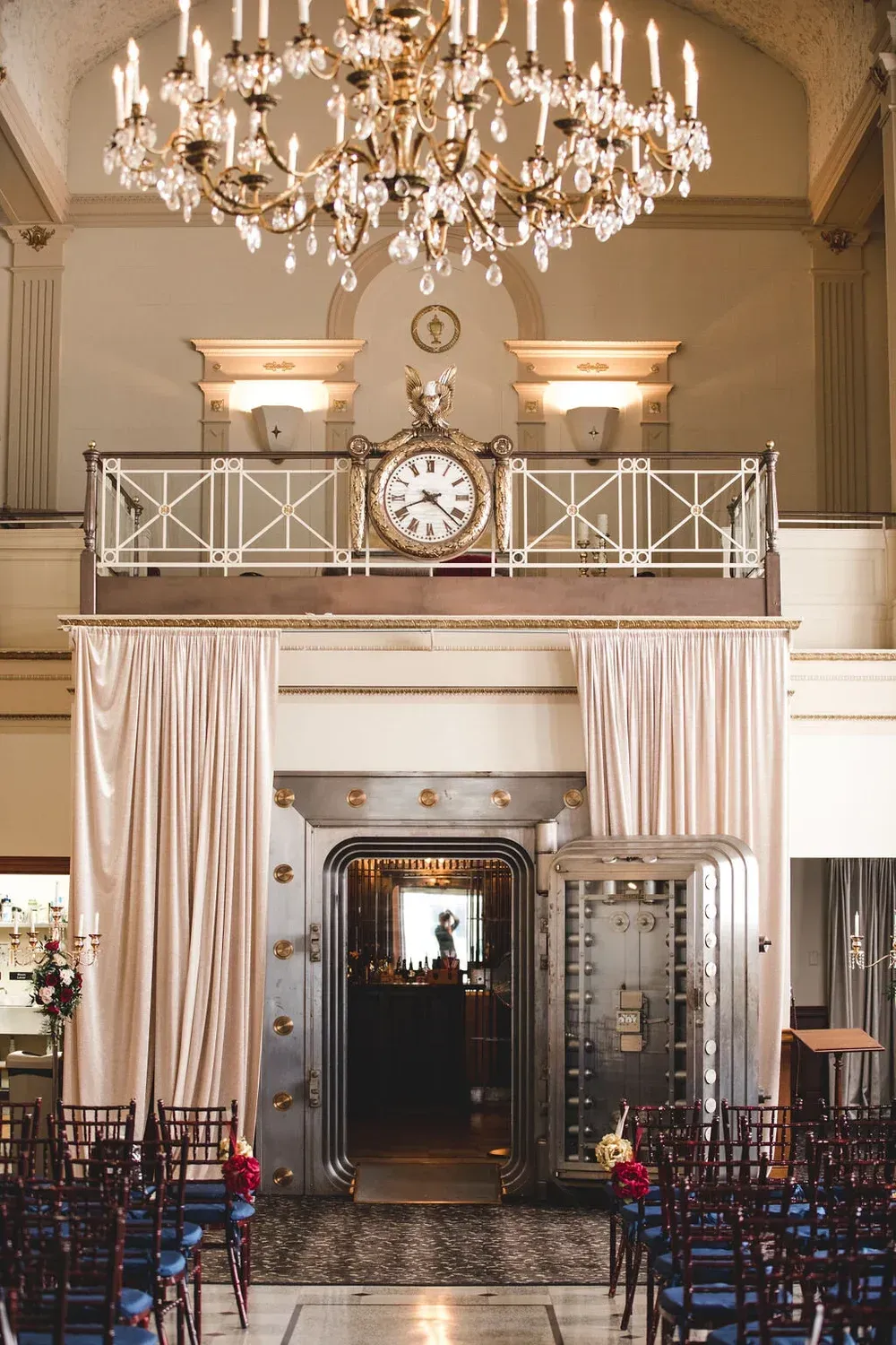 Interior of a venue with a large bank vault as a backdrop for a wedding ceremony; rows of chairs face the vault.