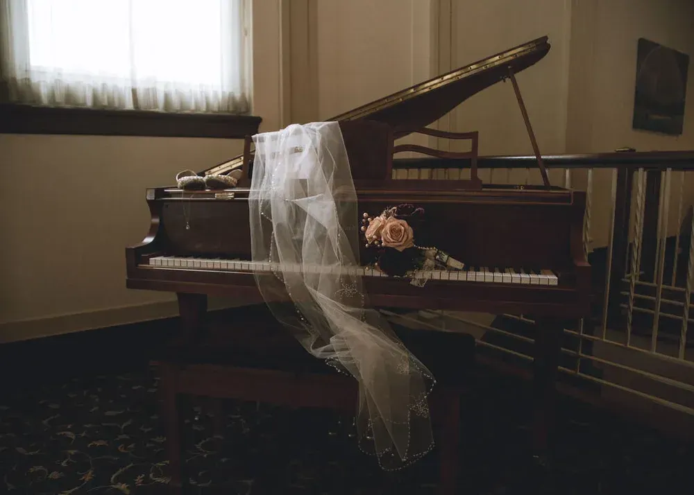 A grand piano draped with a wedding veil and flowers, set in a dimly lit room.