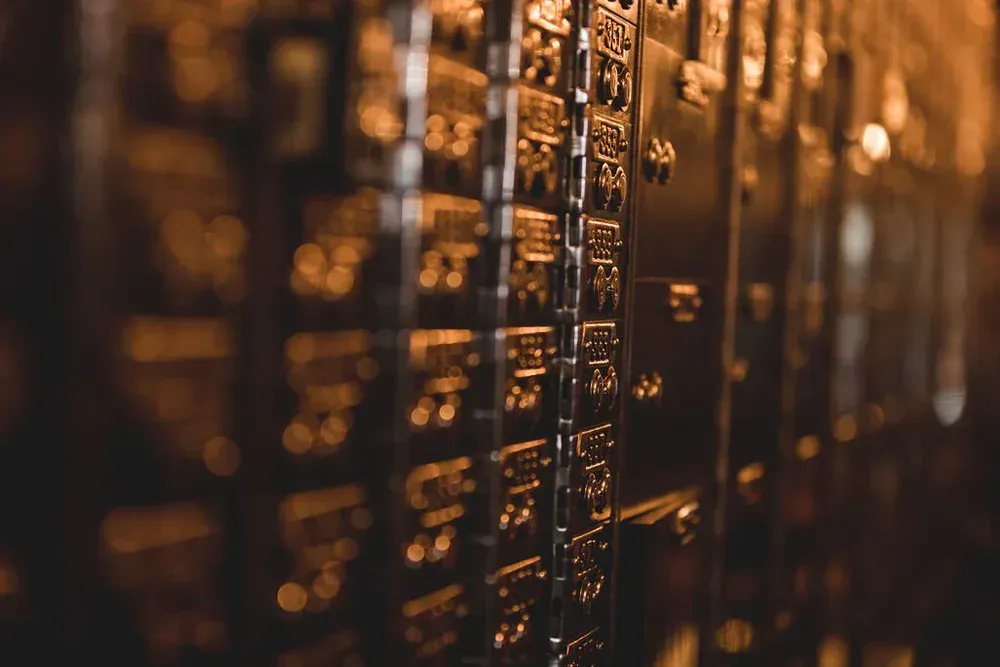 Close-up of a row of dark metal safety deposit boxes in a dim, warm-toned setting.