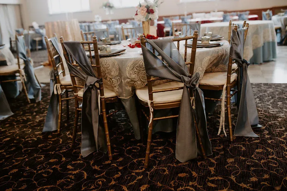 Wedding reception table set with gold chairs tied with gray fabric, round table with floral centerpiece.