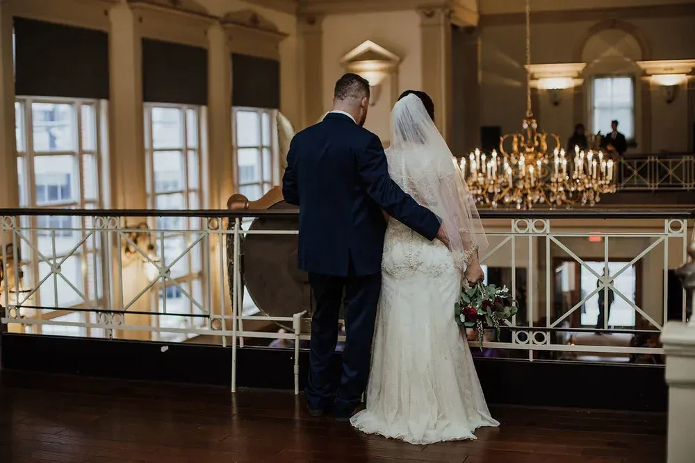 A bride and groom embrace on a balcony overlooking a wedding venue.