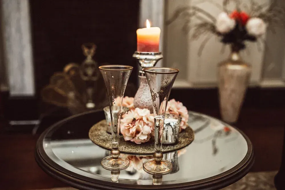 Candlelit centerpiece on a mirrored table, featuring champagne flutes, flowers, and a burning candle.