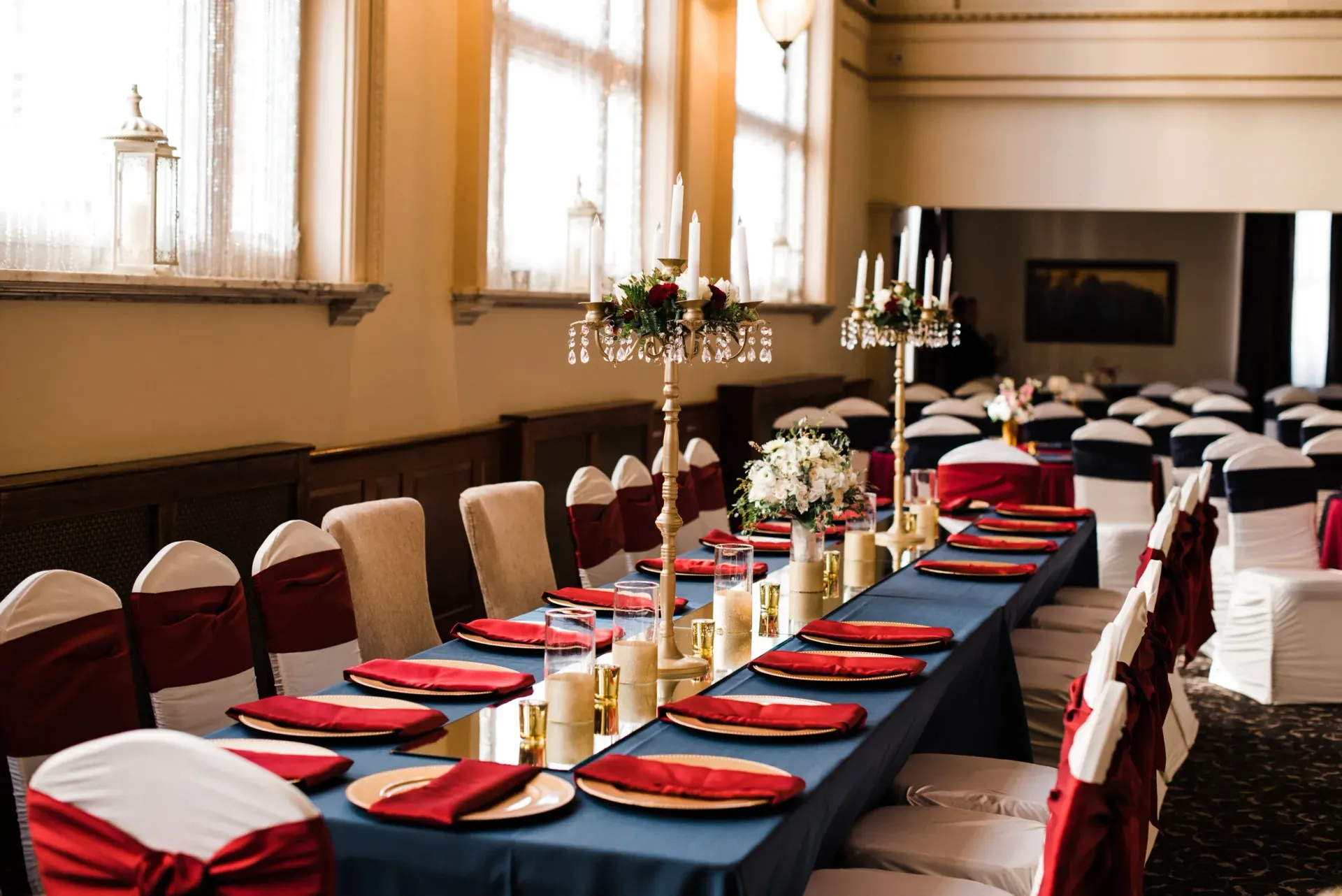 Long dining table set for a formal event, with white chairs and burgundy accents. 