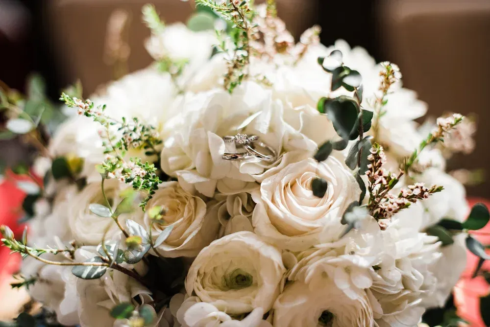 Close-up of a bridal bouquet with white roses and hydrangea, featuring wedding rings nestled among the petals and greenery.