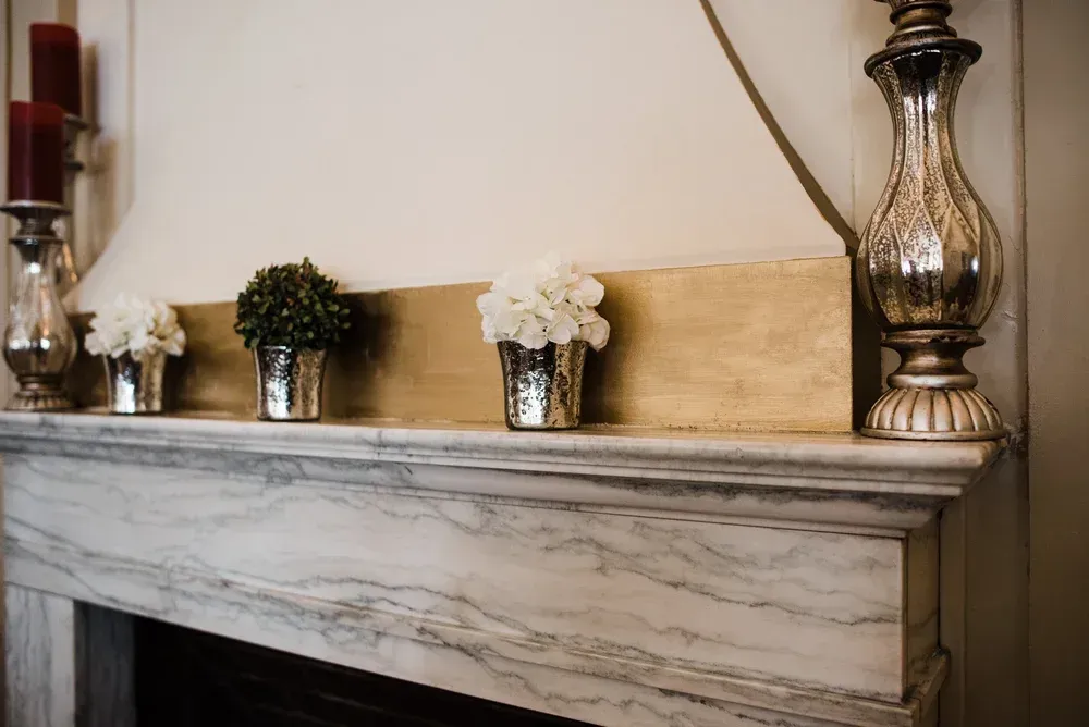 Fireplace mantel with silver and gold accents, holding candles and flower arrangements.