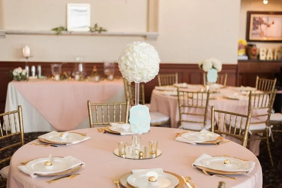 Elegant event tables with pink tablecloths, gold chairs, and floral centerpieces,
