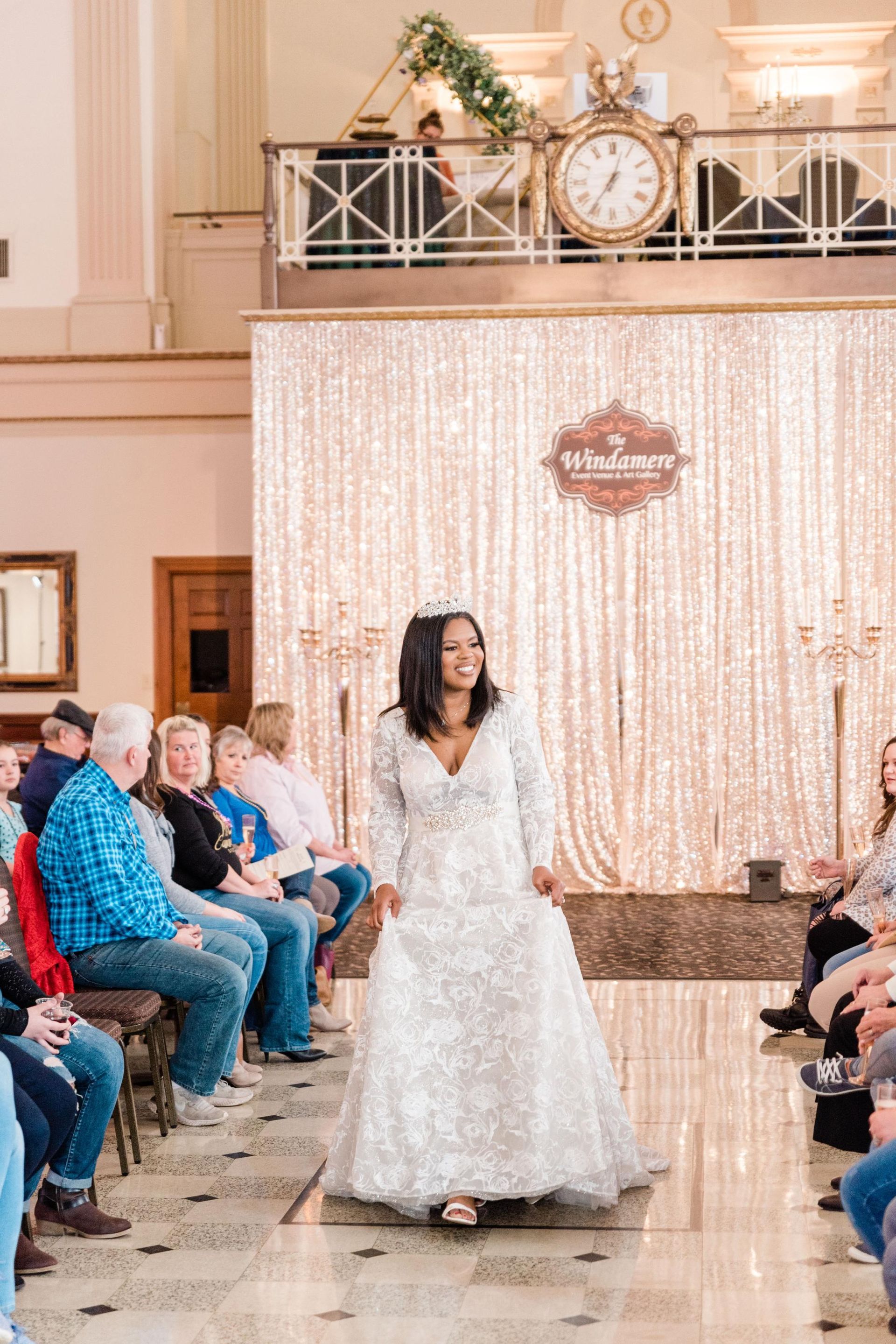 Woman in wedding dress walking a runway at an event, in a large room.