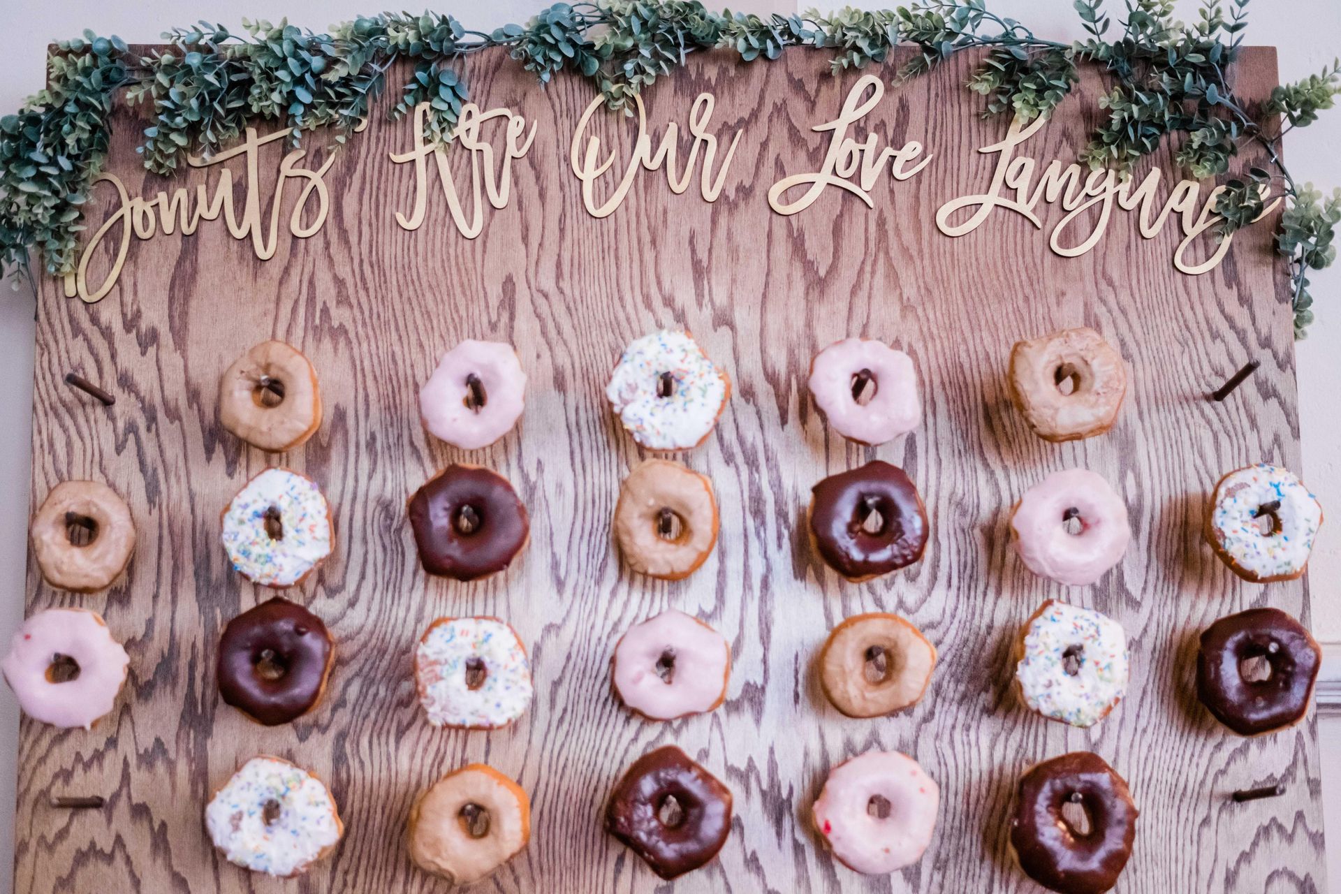 Donut display on wooden board, adorned with greenery and golden cursive text: 