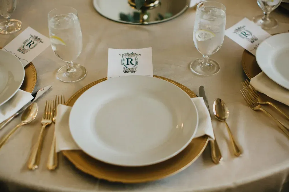 Elegant table setting with gold charger, white plate, gold cutlery, and monogrammed place card.