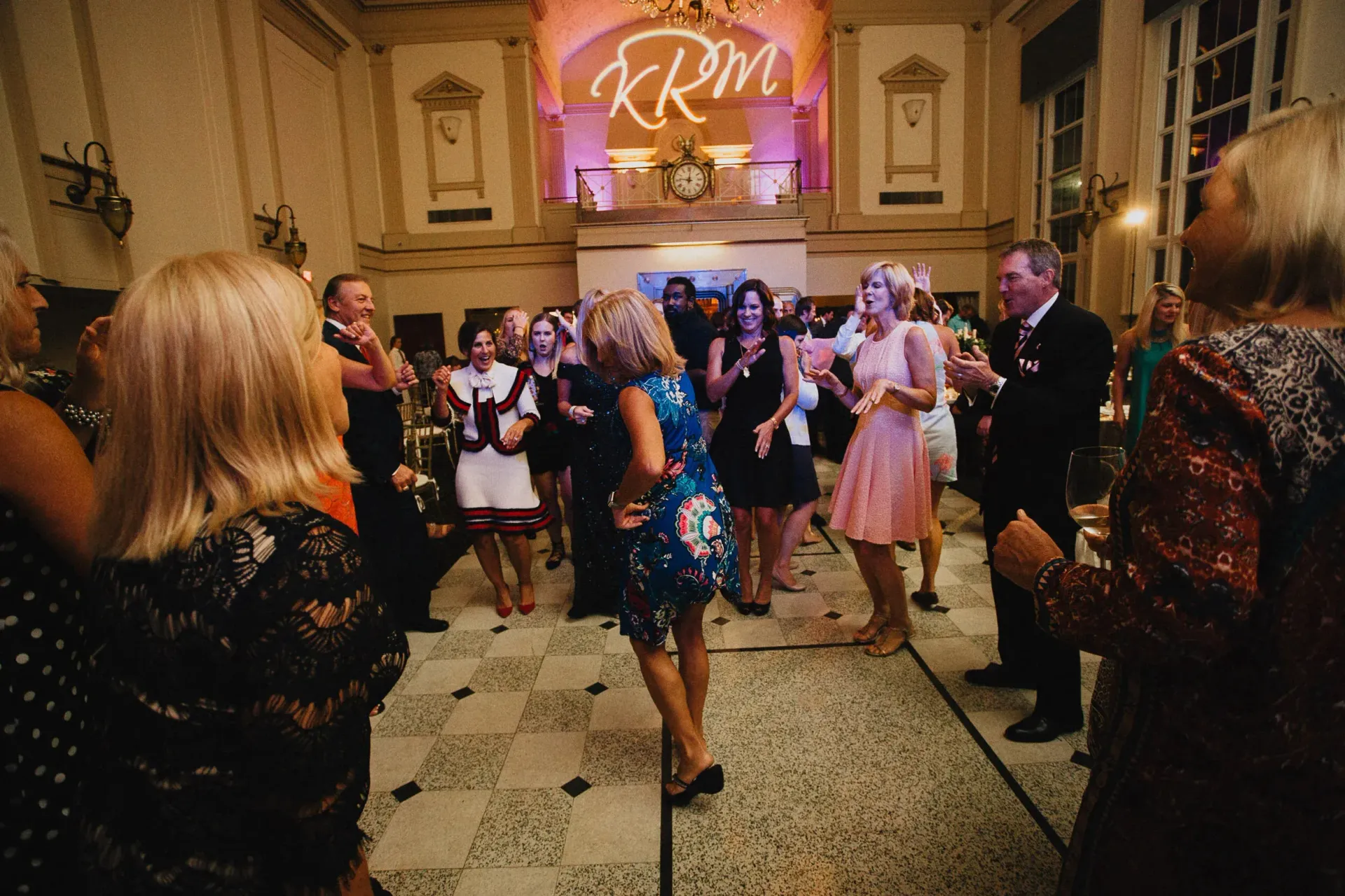 People dancing in a brightly lit ballroom; a sign with 