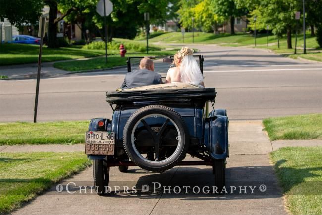 Bride and groom in vintage blue car, driving down a street after their wedding.
