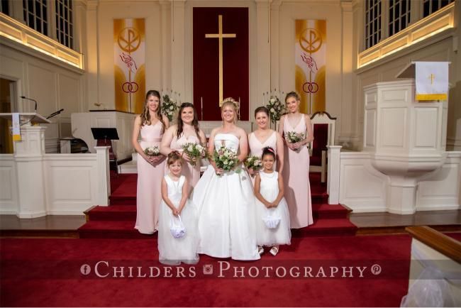 Bride and bridesmaids in pink gowns pose at the altar of a church.