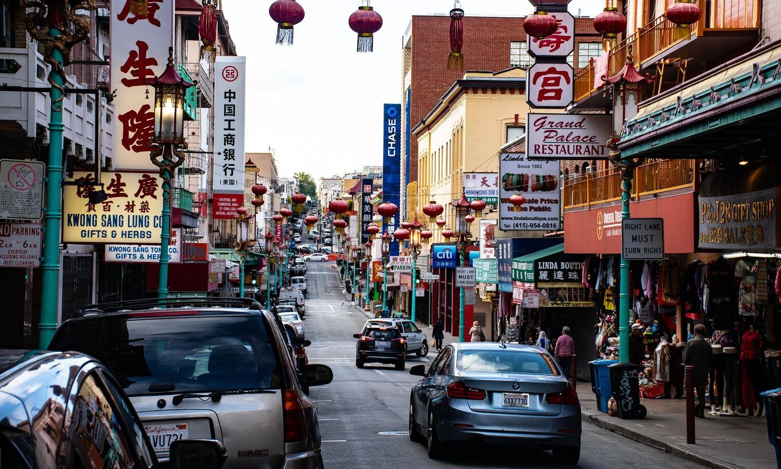 Street scene in Chinatown, San Francisco, with shops, signs, and cars. Red lanterns hang overhead; buildings line the street.