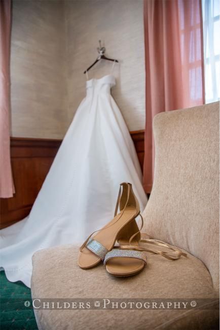 Wedding dress hanging on wall; beige shoes on a chair.