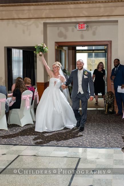 Bride and groom exiting ceremony, bride raising arm. They walk toward exit, other guests follow.