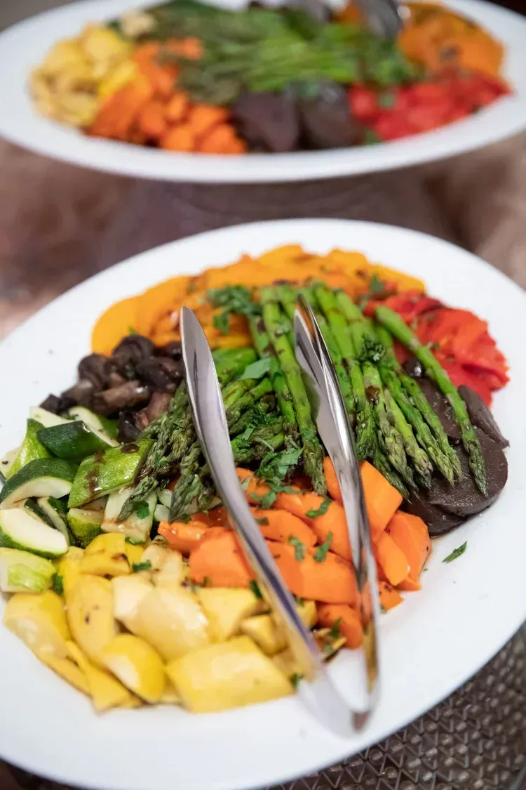 Platters of roasted vegetables, including asparagus, carrots, squash, and mushrooms, arranged on white plates.