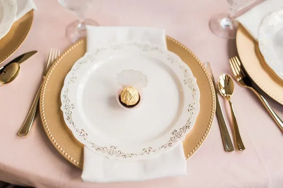 Elegant place setting with gold charger, white plate, napkin, and gold cutlery. A chocolate candy sits on the plate.