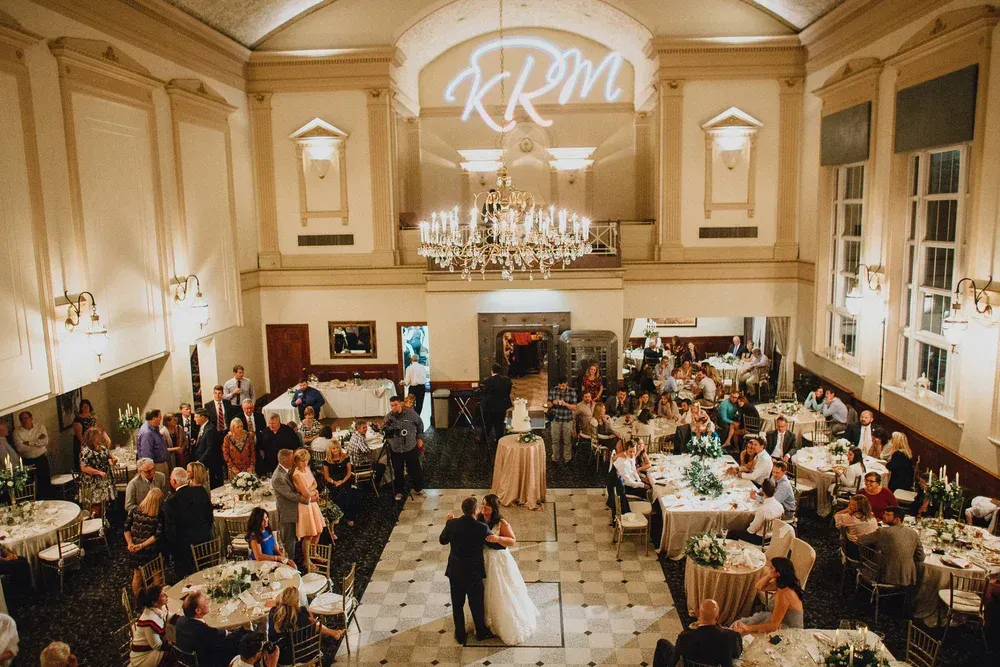 Wedding reception. A couple dances in a ballroom with guests seated at round tables.