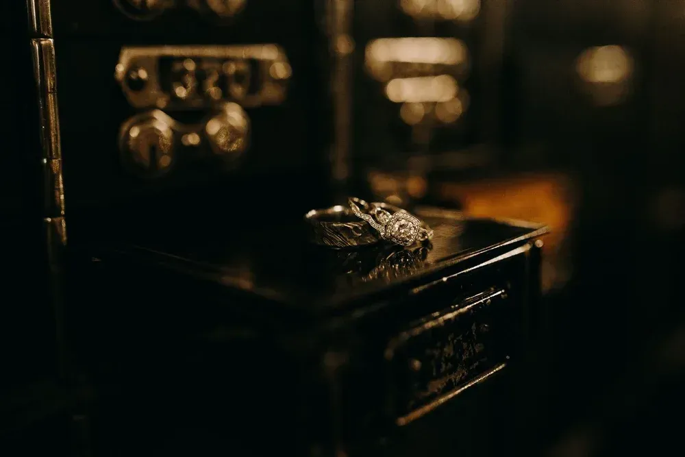 A silver ring with detailed carving rests on a dark box with ornate details, lit by warm, focused light.