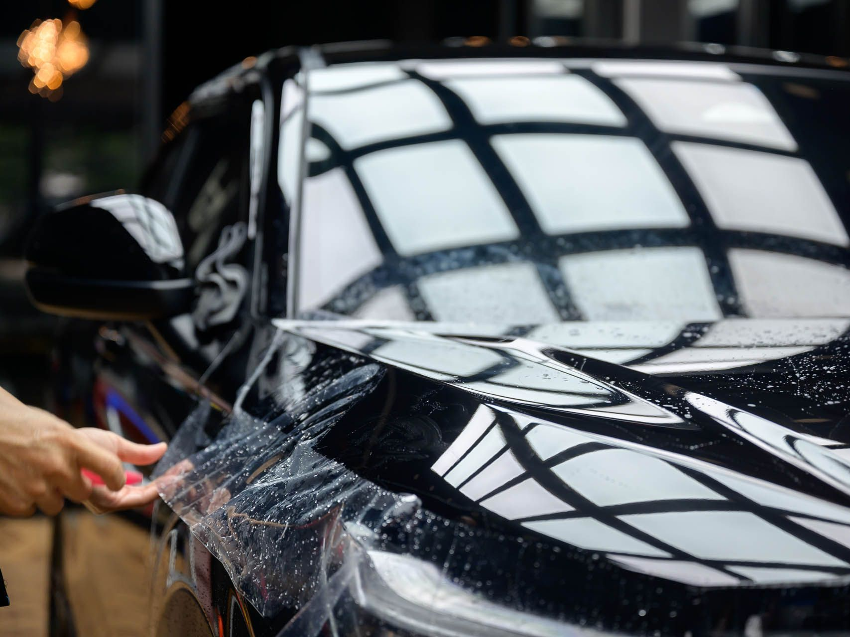 A man is washing a car with a hose in front of a garage door.