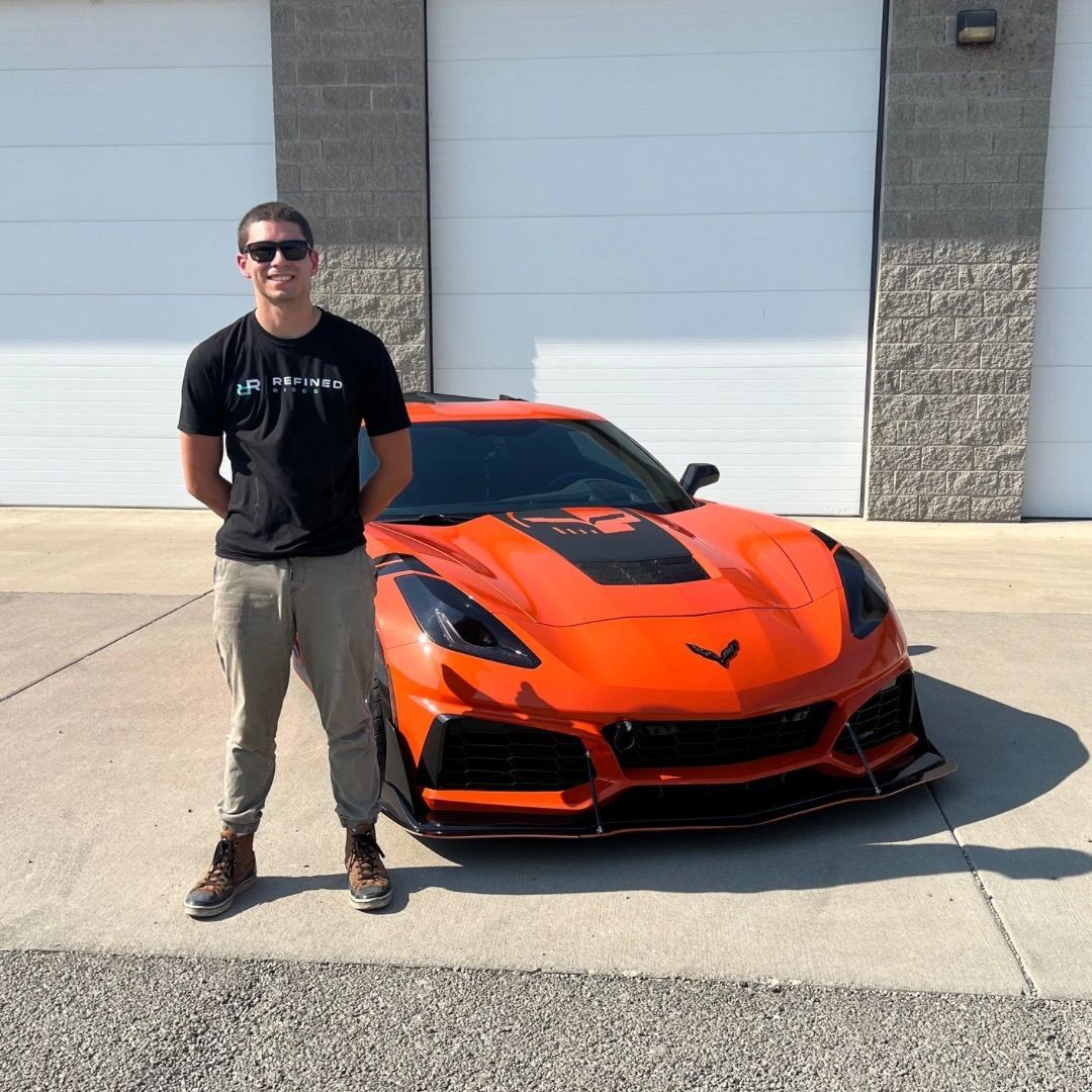 Man in front of an orange sports car, standing in front of garage doors.