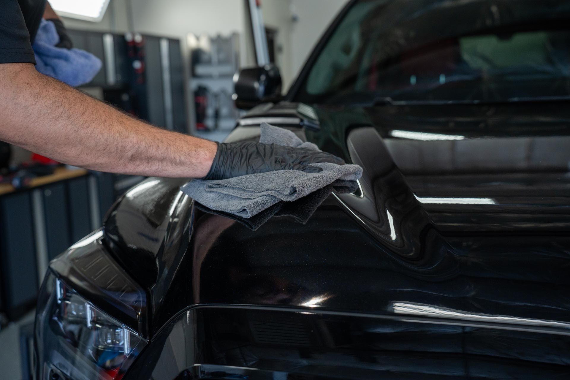 A man is cleaning the hood of a black car with a towel.