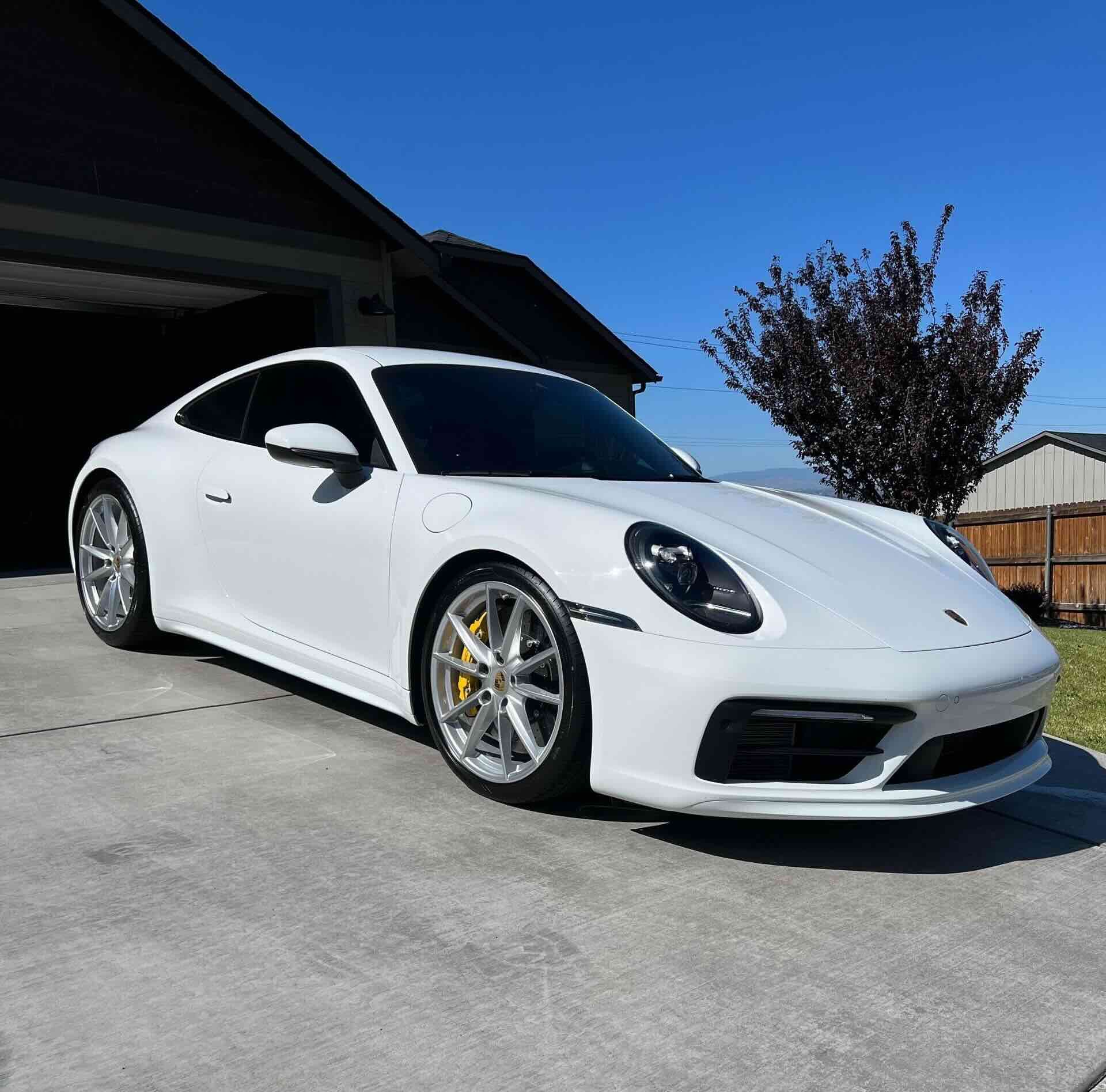 a white porsche 911 is parked in front of a house