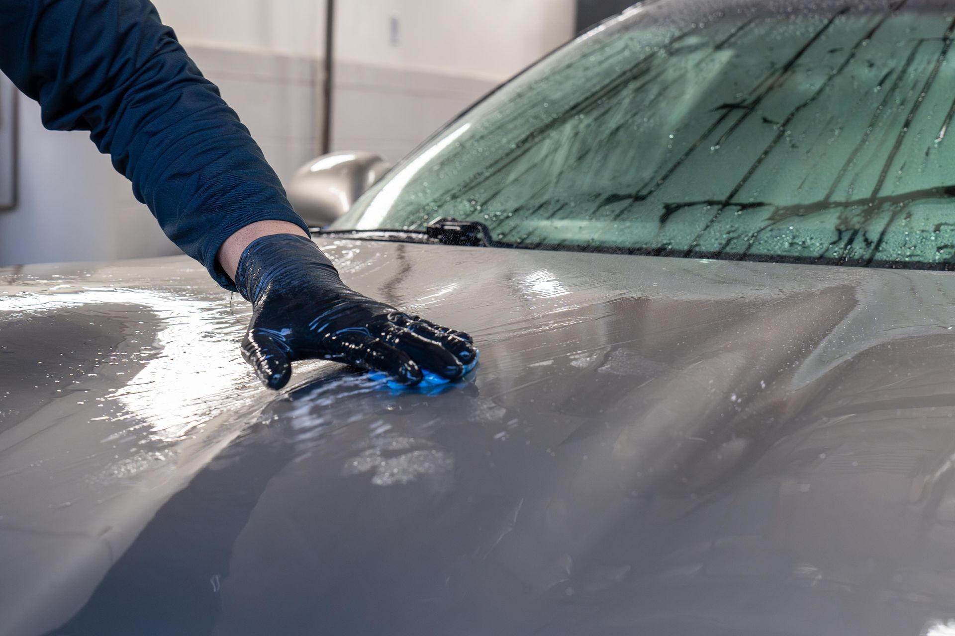 A person is cleaning the hood of a car with a sponge.