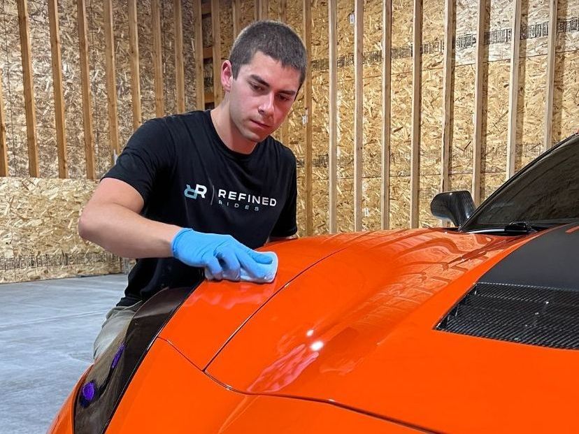 A man is polishing the hood of an orange sports car.