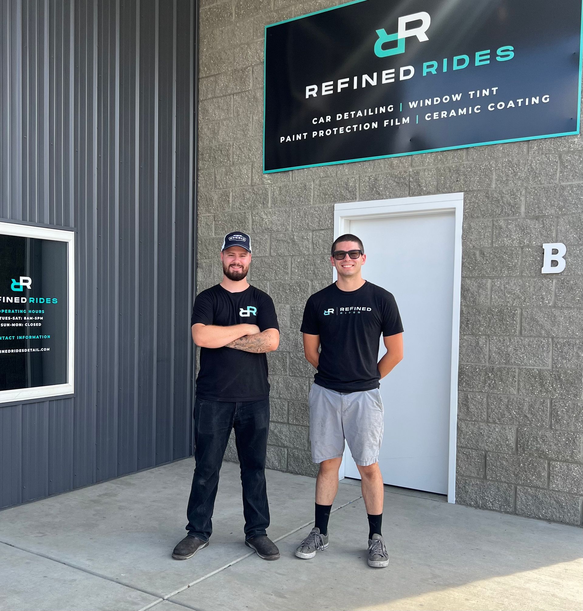 Man polishing a shiny black car, wearing a black t-shirt, shorts, and glasses.