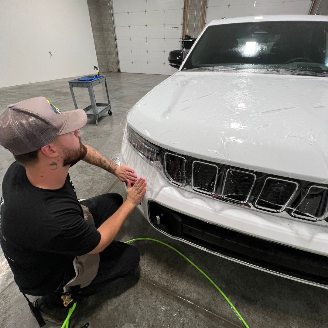 A man is washing a car with a hose in front of a garage door.