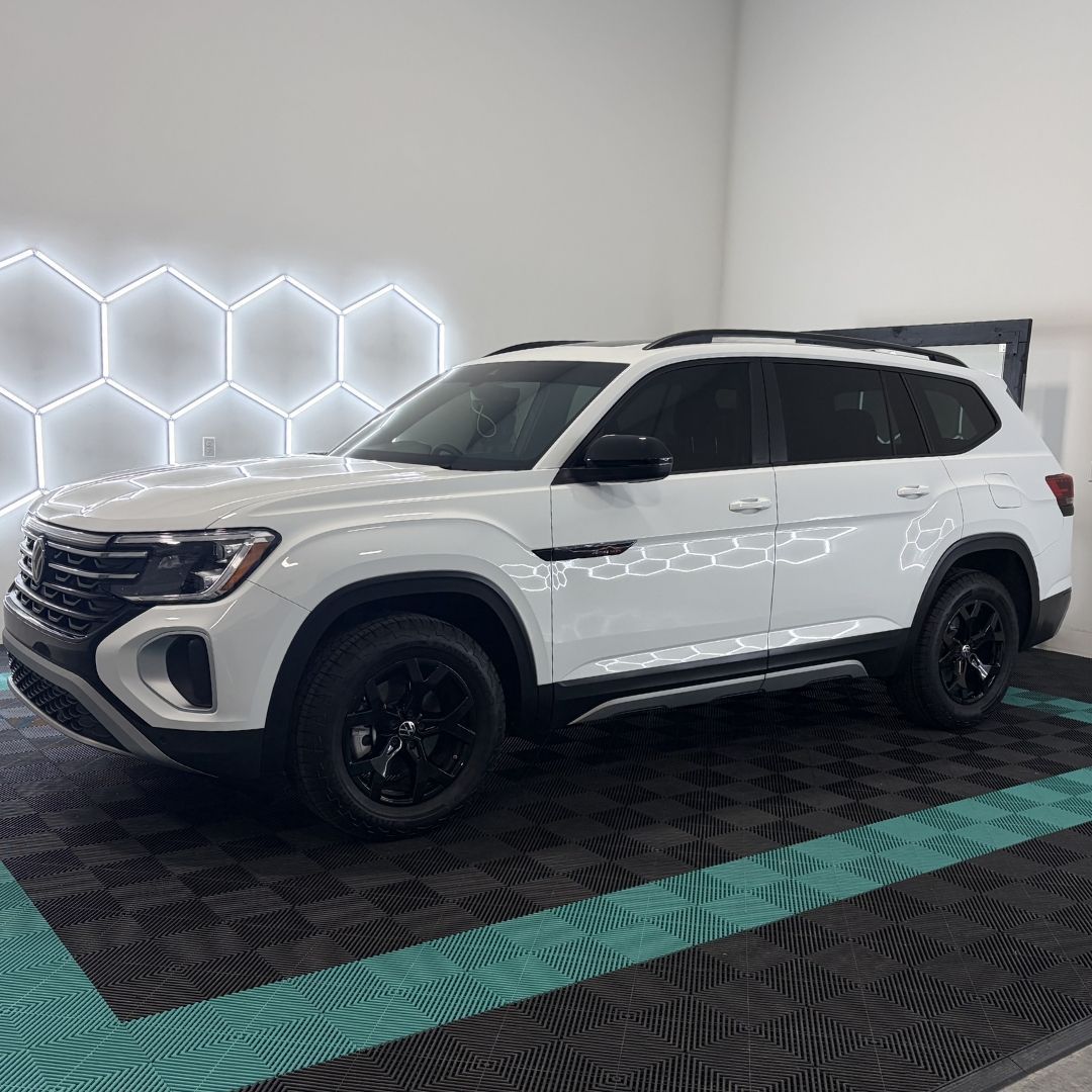 A white Volkswagen Atlas SUV with black wheels parked in a showroom with illuminated hexagon wall panels.