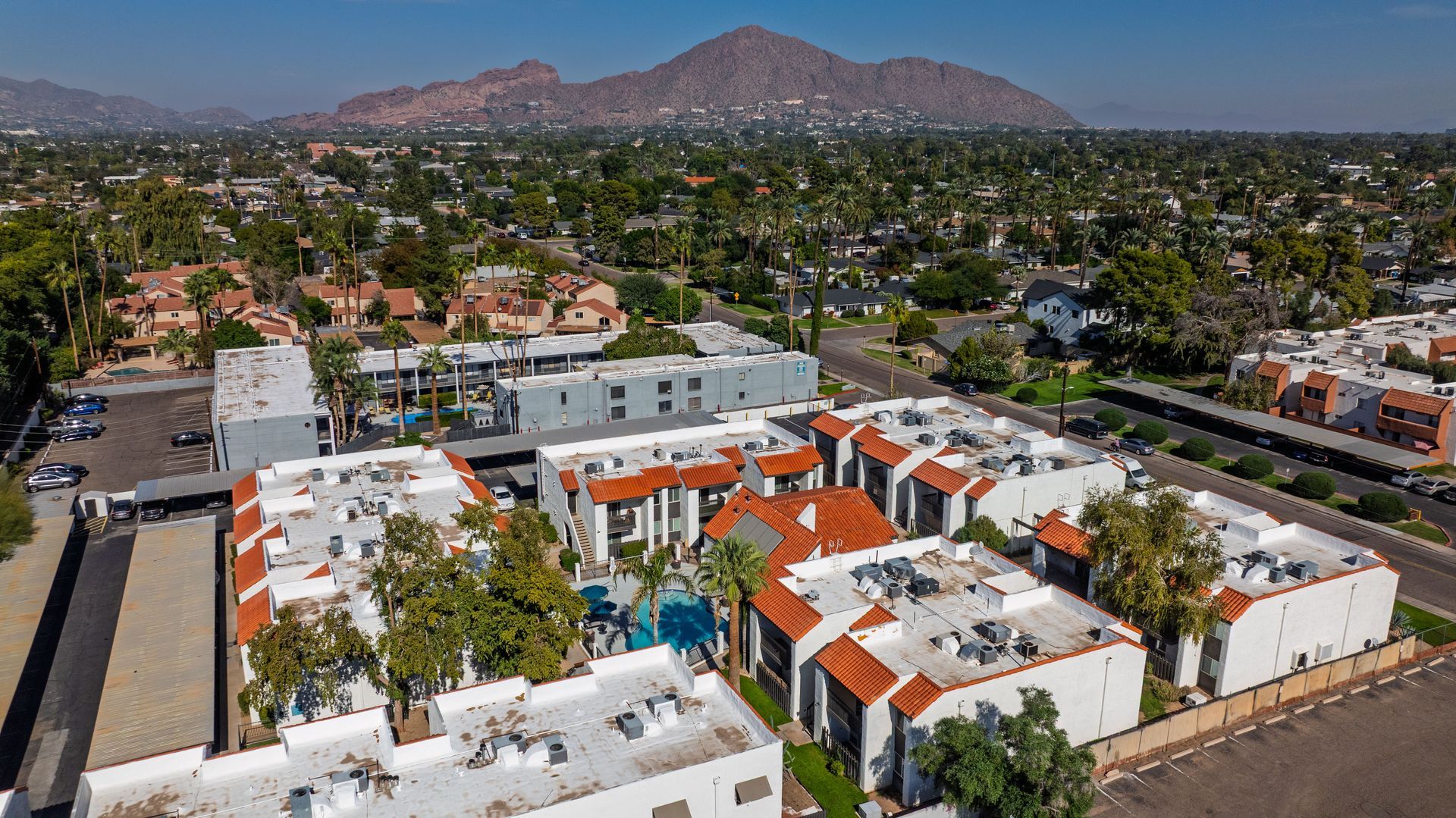 Aerial view of apartments with orange tile roofs, trees, and a mountain in the background.