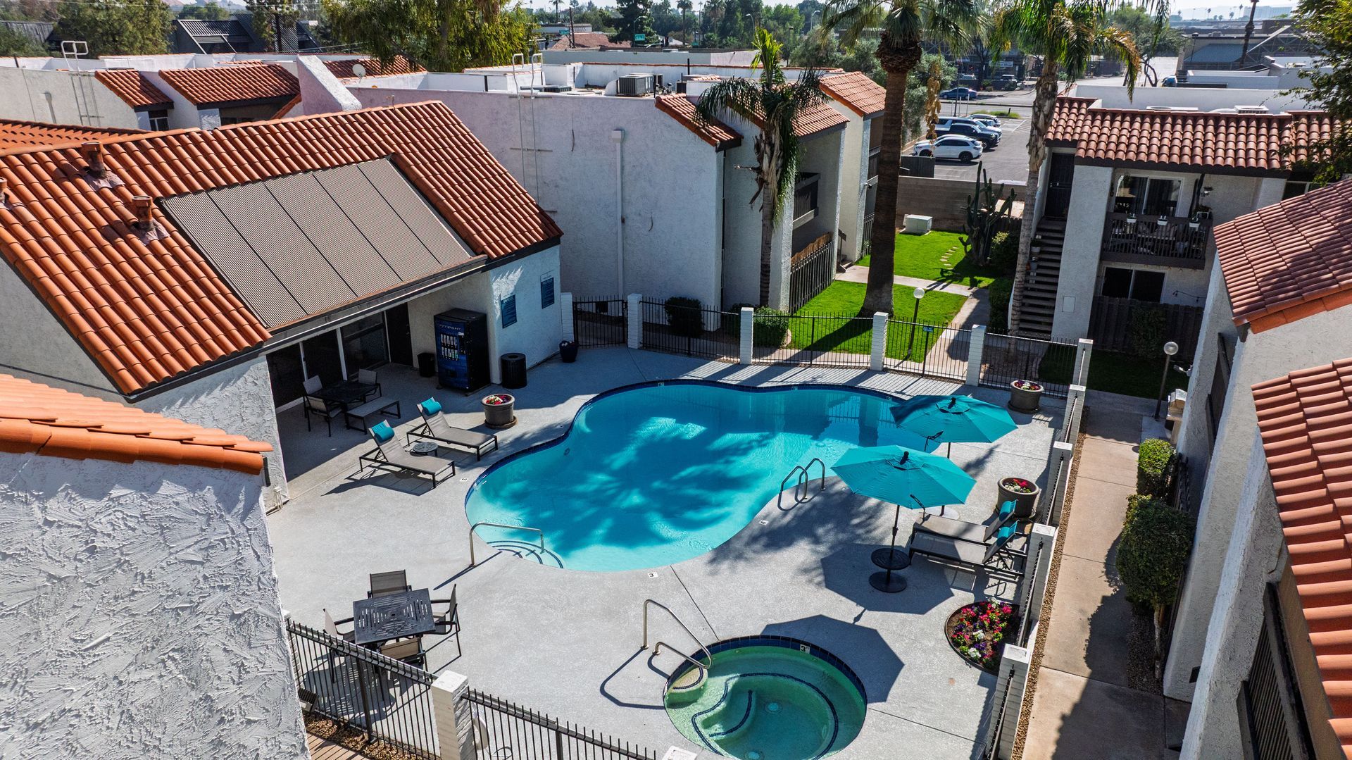 Pool surrounded by buildings with red tile roofs. Blue water, patio furniture, and palm trees.